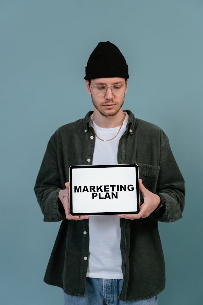 creative Adult wearing casual clothing holding a tablet that reads 'Marketing Plan'.